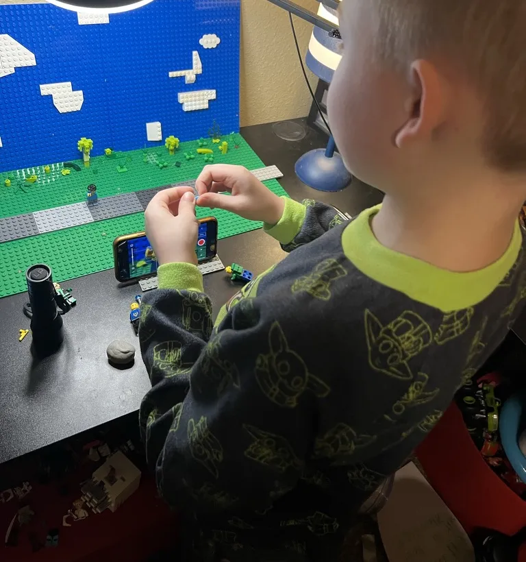 CJ placing a figure on a brick set with a blue sky backdrop while his phone records